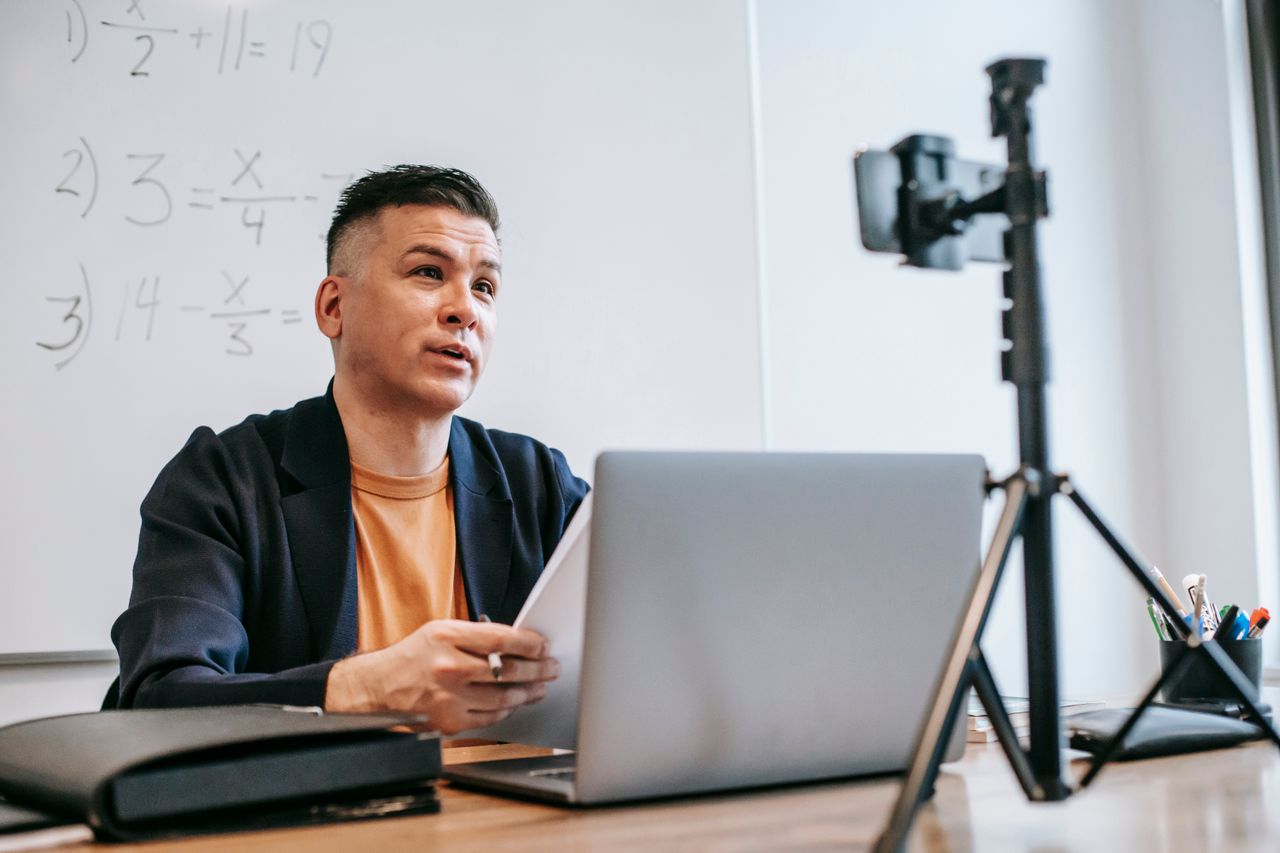 Male instructor conducting an online education session with a laptop and camera.